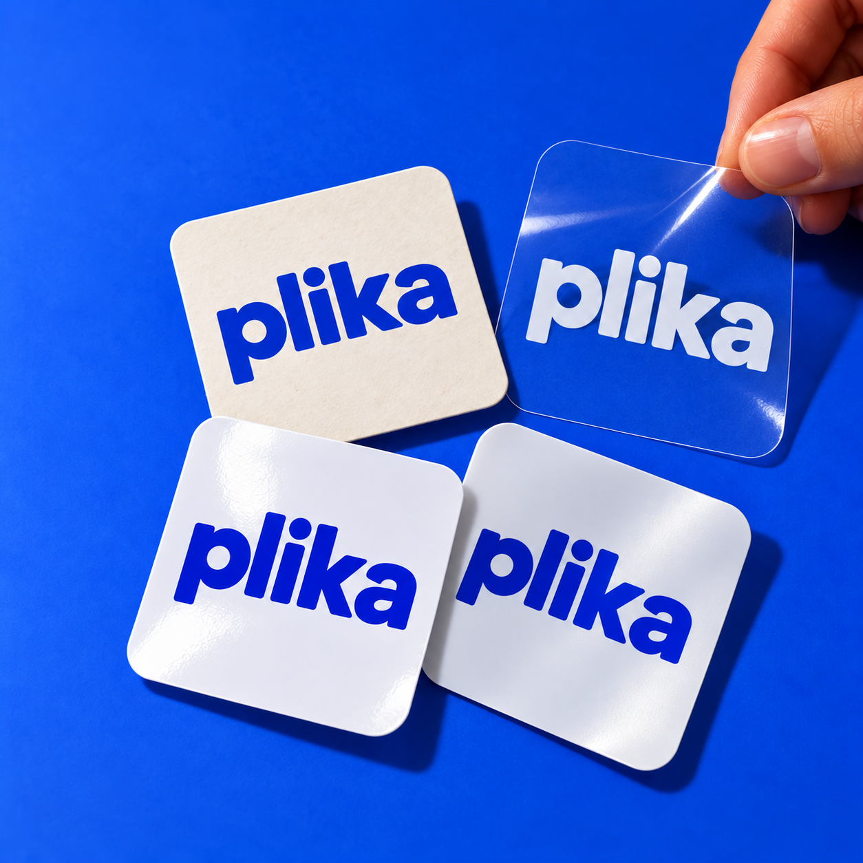Cuatro etiquetas Plika con distintos acabados sobre fondo azul, incluida una transparente sostenida con la mano.